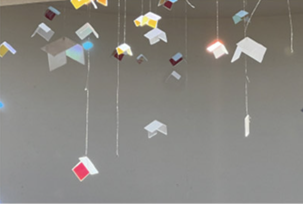Hanging mobile with geometric shapes in various colors suspended by strings against a neutral background.